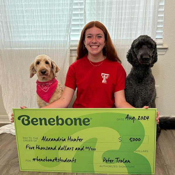 Benebone Scholarship recipient Alexandria Hunter holding a giant green check while sitting next to her dogs.