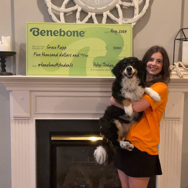 Benebone Scholarship recipient Grace Rapp standing next to a giant green check while holding her dog.