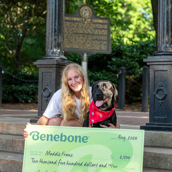 Benebone Scholarship recipient Maddie Franz holding a giant green check while sitting next to her dog.